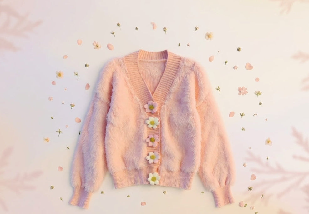 Pastel striped cardigan with floral buttons on a soft pink background, labeled 'Cozy Knits'.