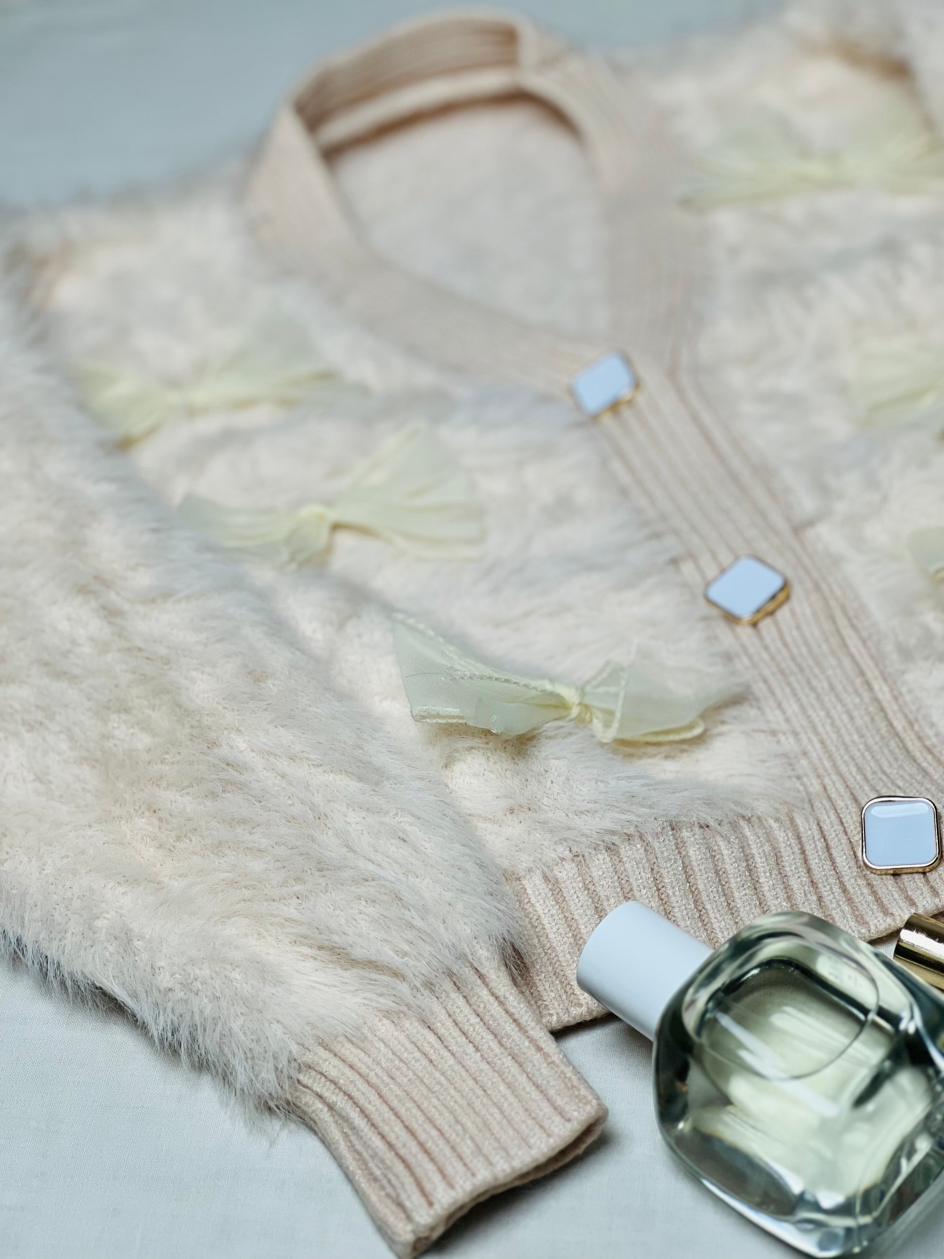 Fluffy beige woollen cardigan in soft fur fabric with bow embellishments.